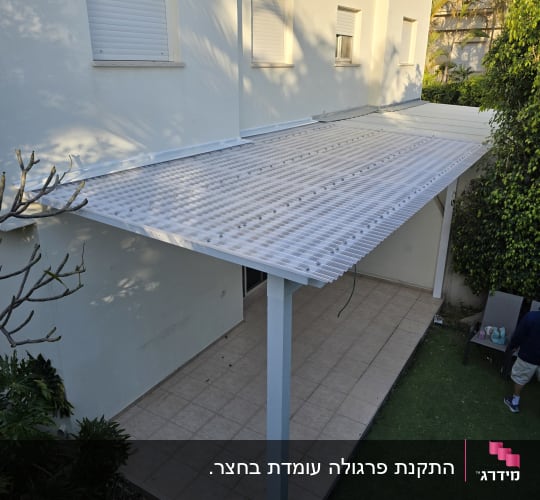פרגולה לבנה מעל מרפסת מרוצפת ליד בית